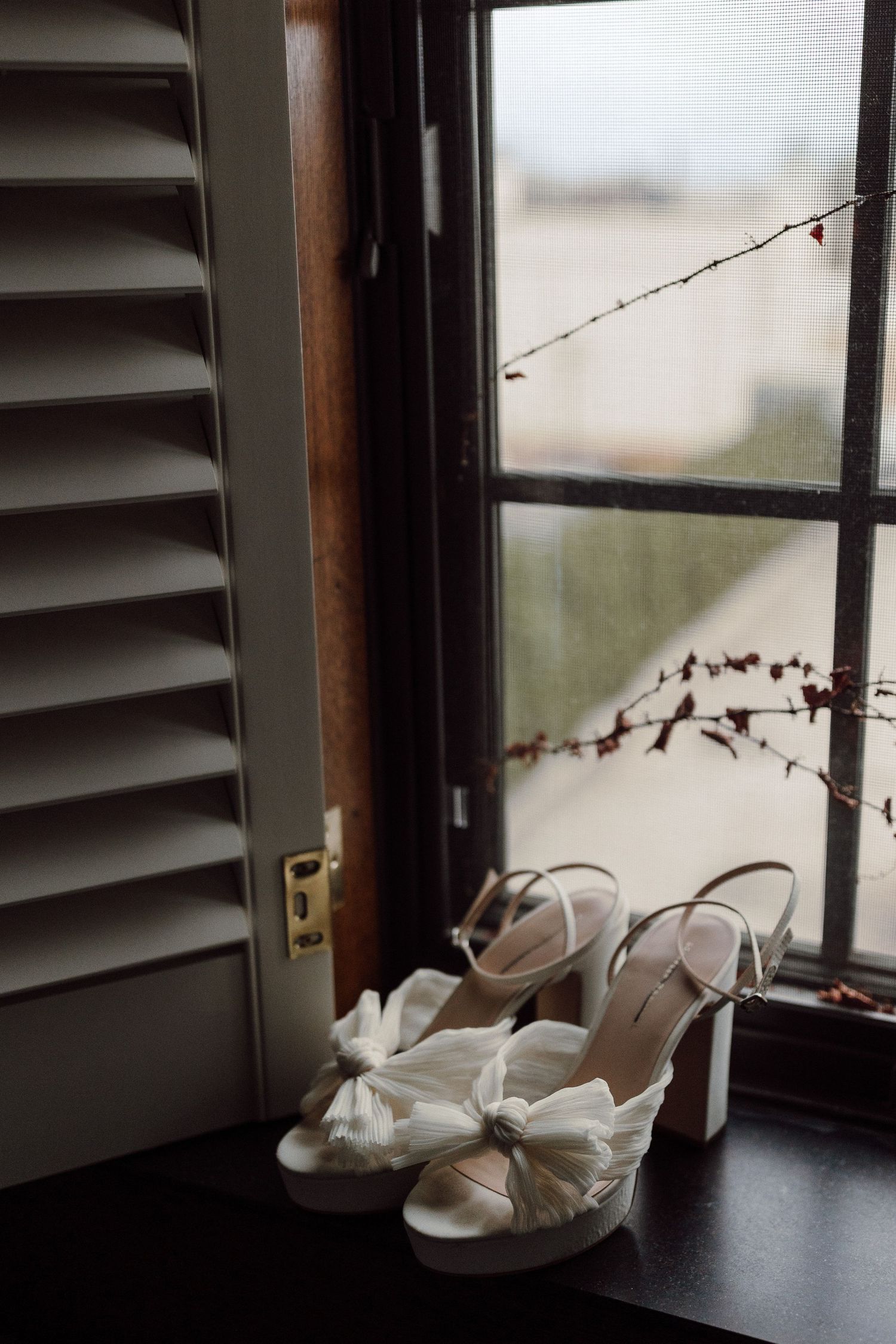 White bridal heels with bow detail displayed on windowsill with soft natural light.