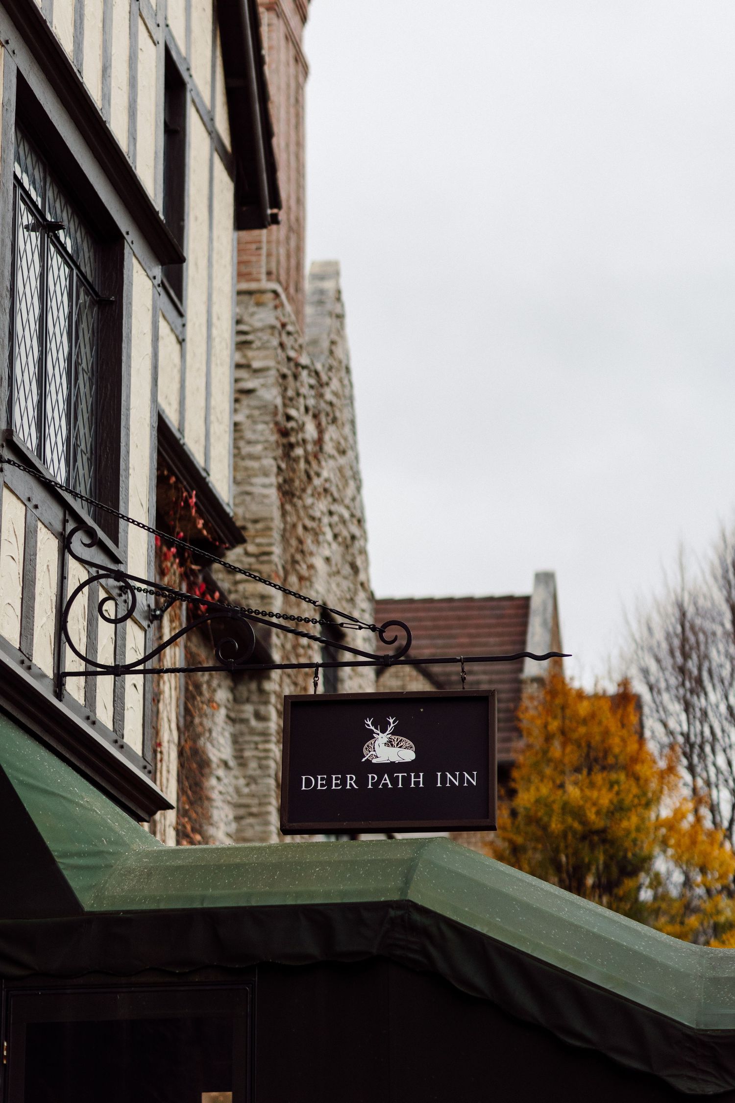 Deer Path Inn sign mounted on ornate iron bracket on historic Tudor-style building exterior in autumn.