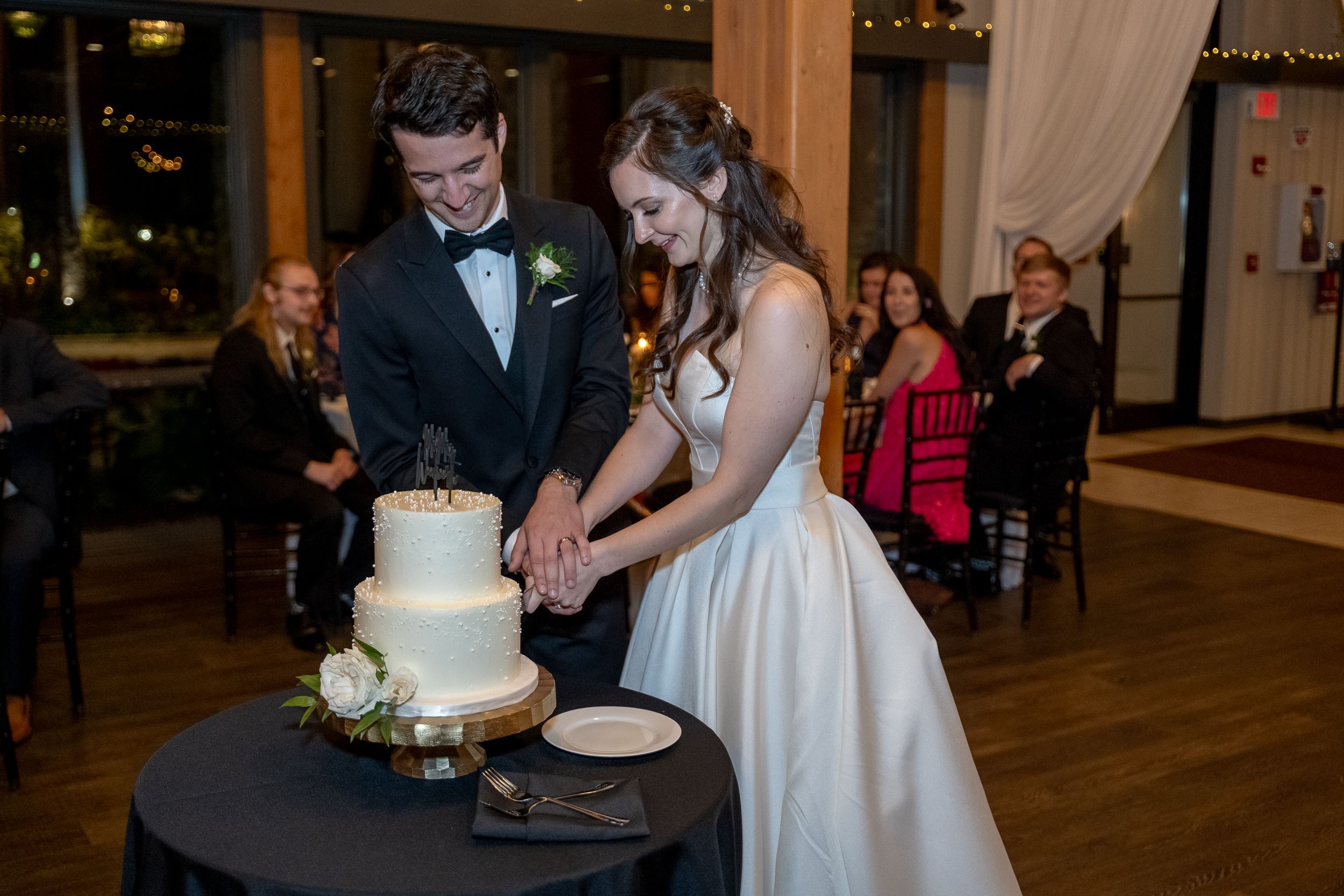 Bride and groom cutting their white wedding cake together at a elegant indoor wedding reception.