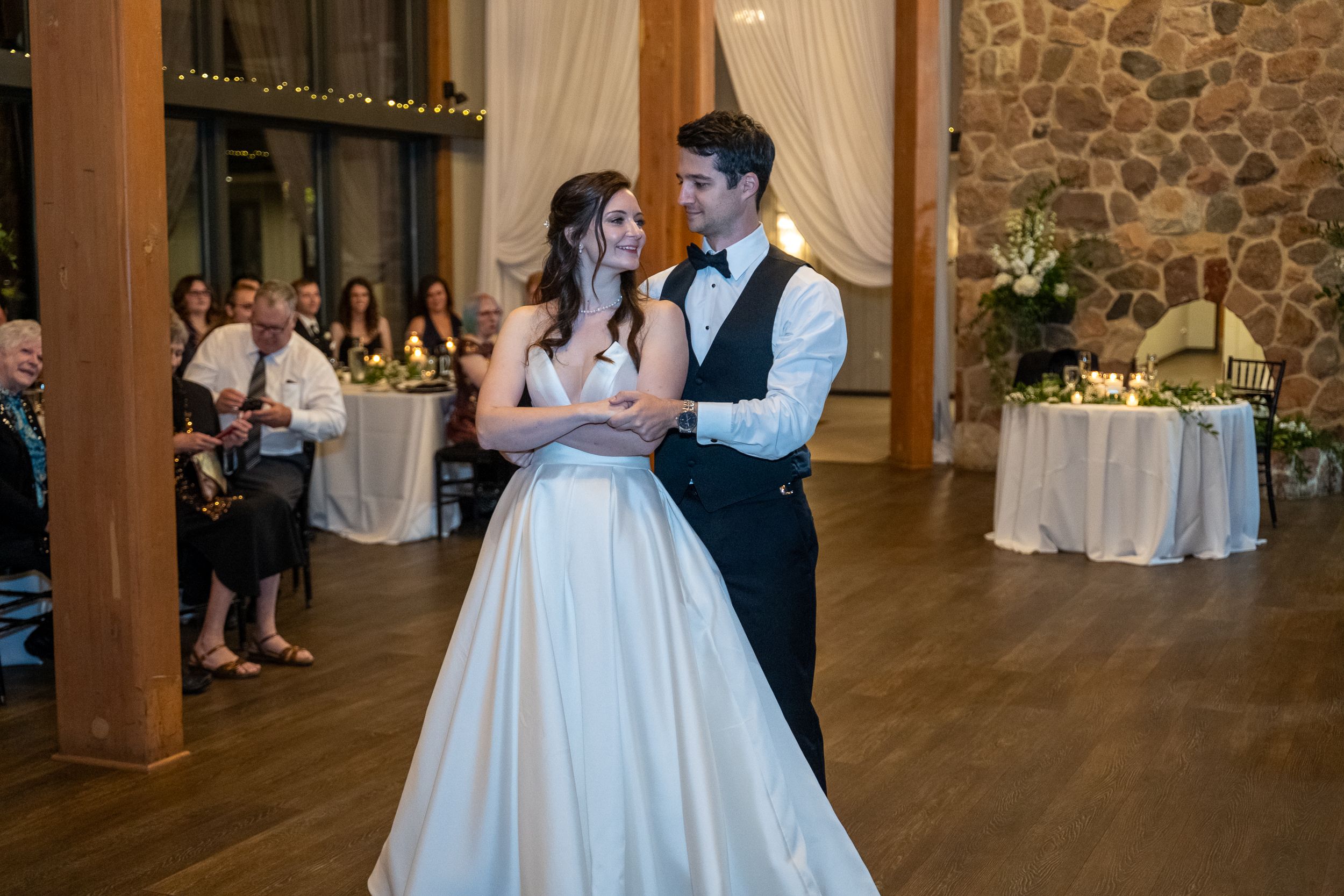Bride and groom share their first dance at a rustic wedding reception venue with stone walls and warm lighting.
