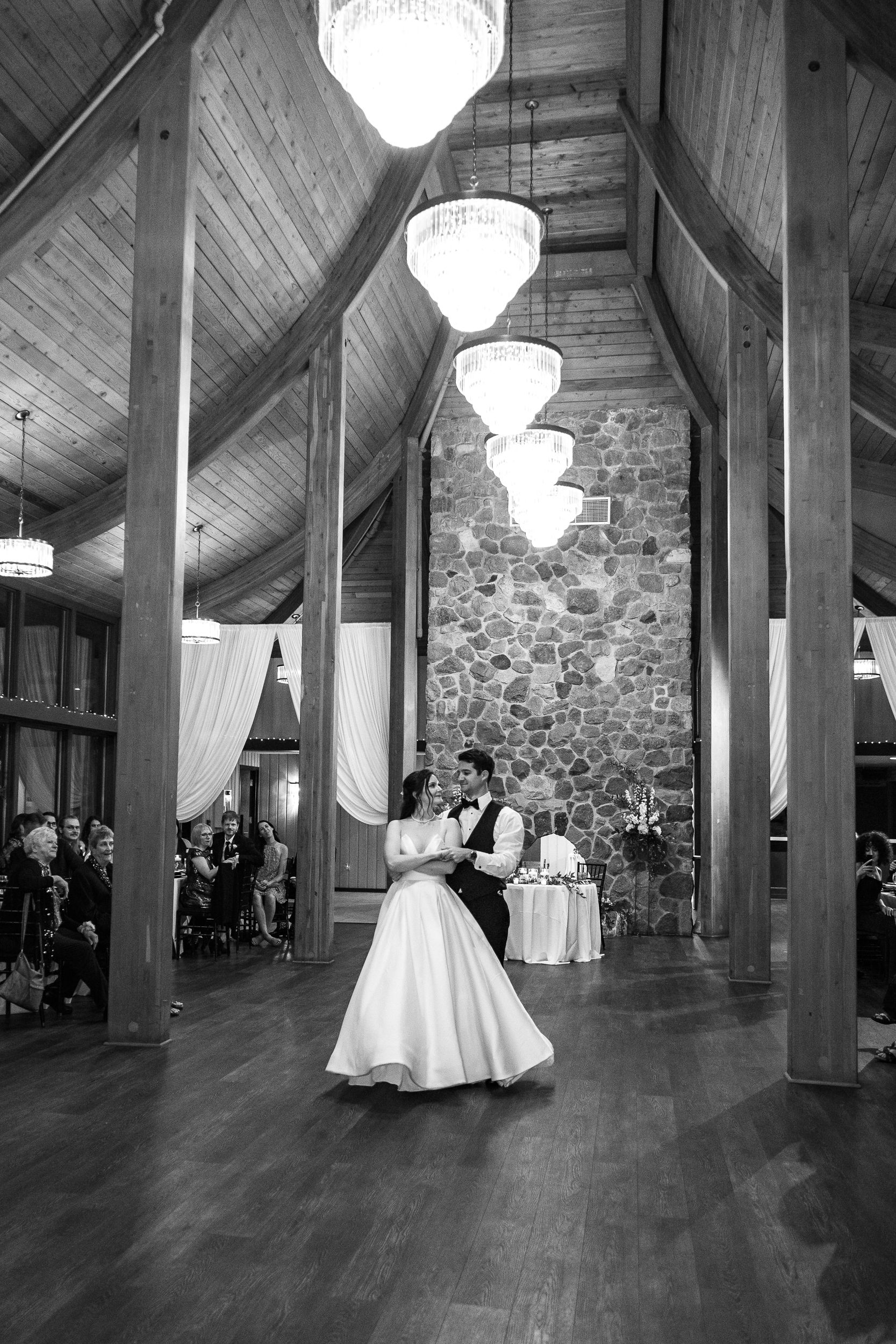 Bride and groom share their first dance in an elegant rustic barn venue with chandelier lighting and stone walls.