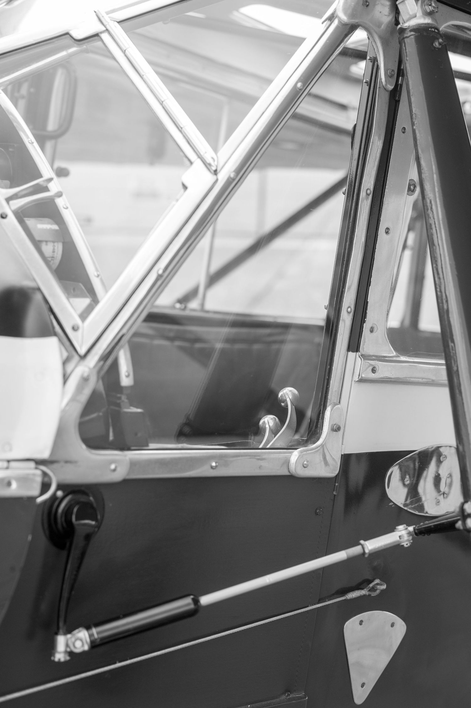 Black and white close-up of a vintage aircraft cockpit door with chrome hardware and riveted metal panels.