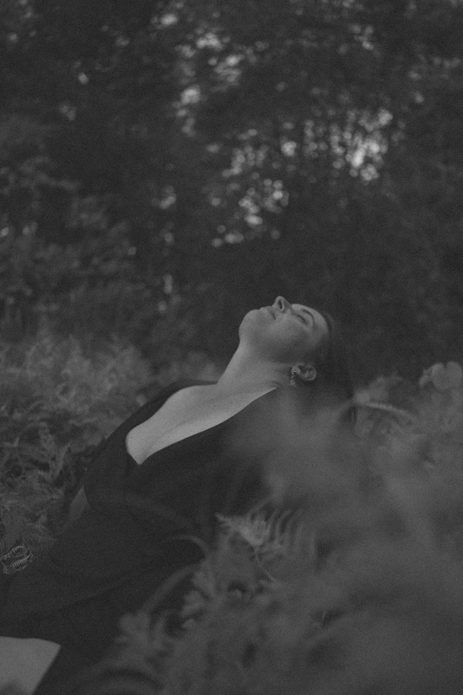 Black and white photo of a woman with head tilted back among lush foliage outdoors in New Zealand.
