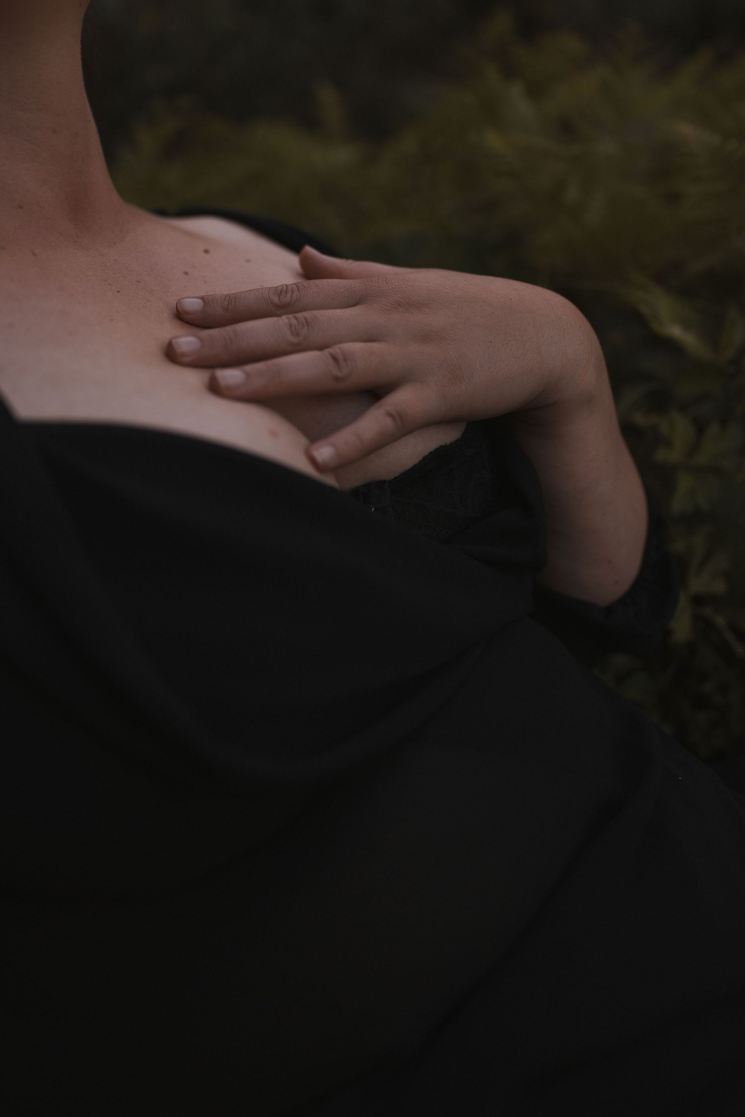 Close-up of a woman's hand resting on her chest wearing a black off-shoulder dress outdoors in New Zealand.