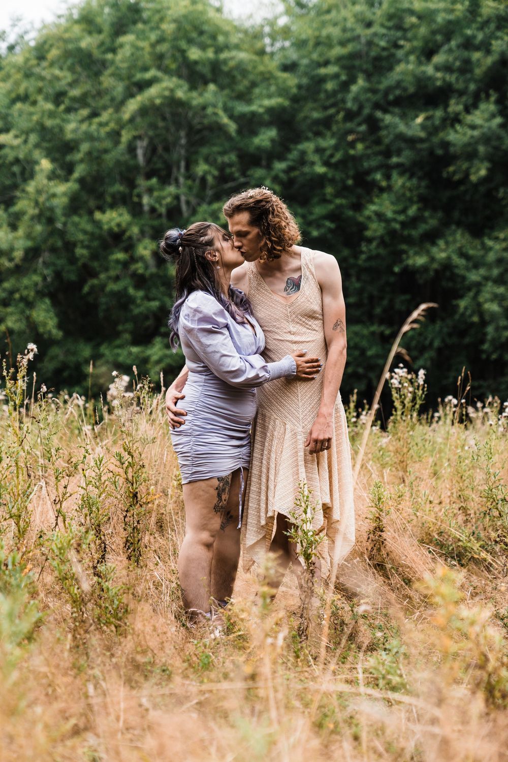 Couple sharing a romantic moment kissing in a wildflower field with lush green trees in the background.olympic national park elopement