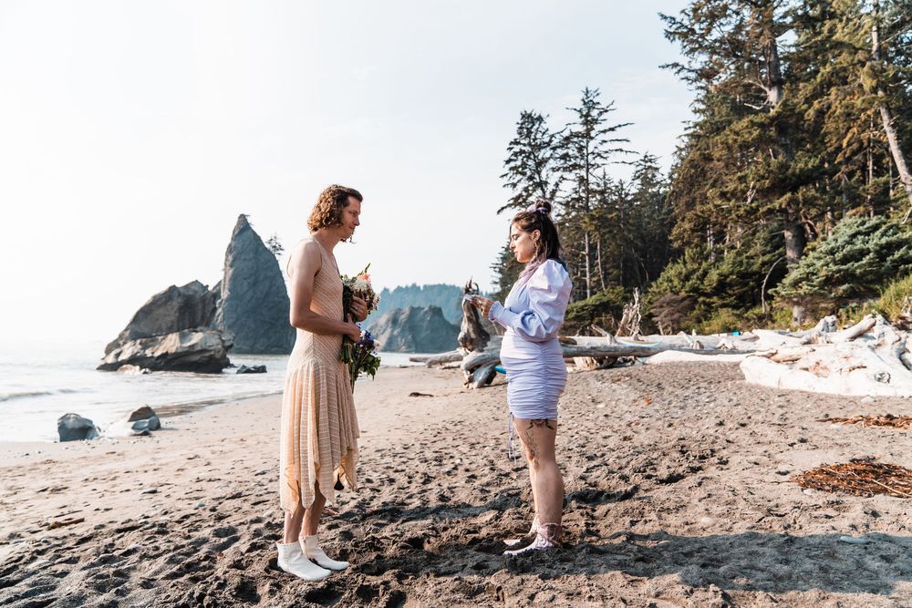 Two brides exchange vows on a scenic Pacific Northwest beach surrounded by sea stacks and evergreen trees. olympic national park elopement