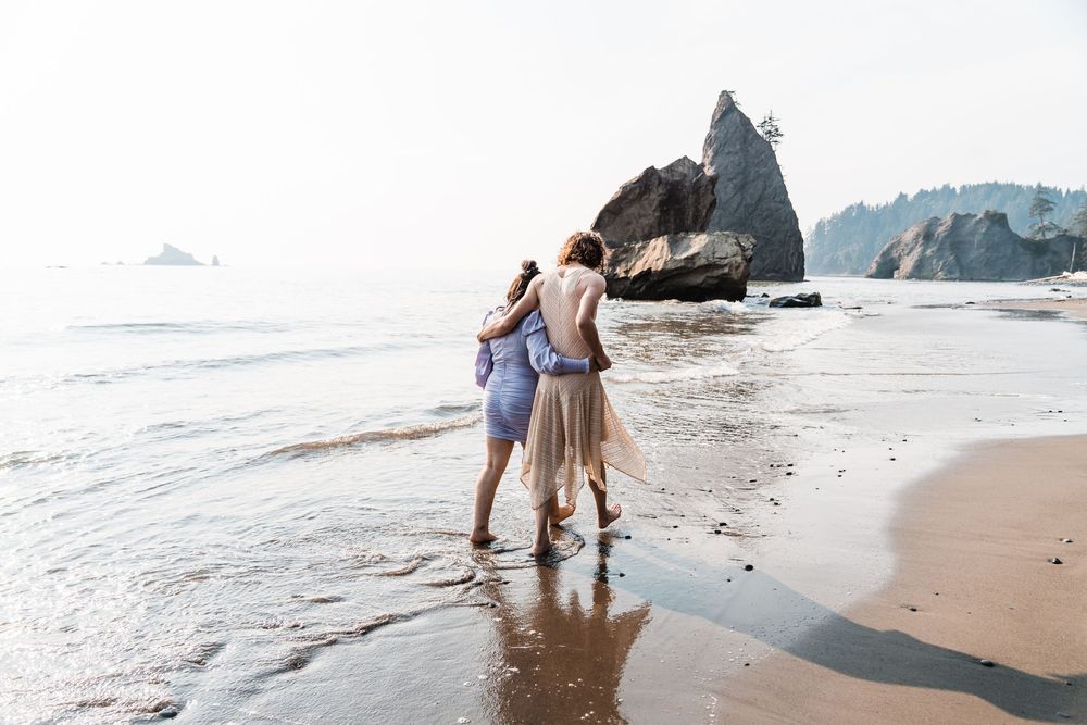Couple walking barefoot on a misty beach with rocky sea stacks, embracing in a romantic coastal scene. olympic national park elopement