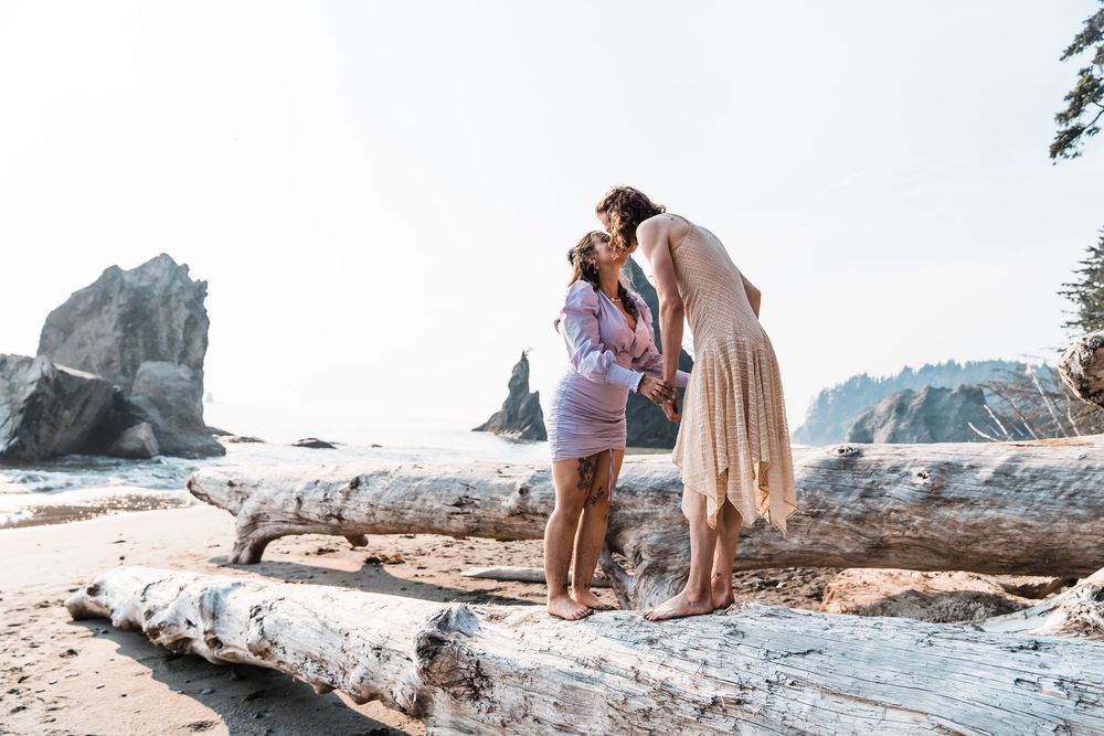A couple shares a romantic moment standing on driftwood during a beach wedding photoshoot. olympic national park elopement