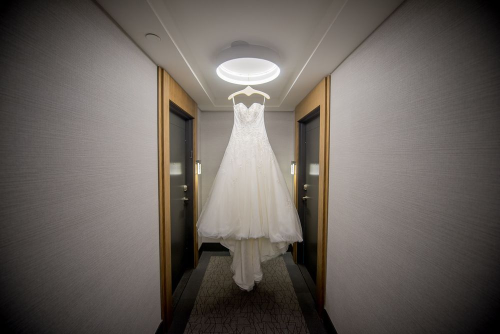 Elegant white wedding gown hanging in hotel hallway under ceiling light before ceremony.