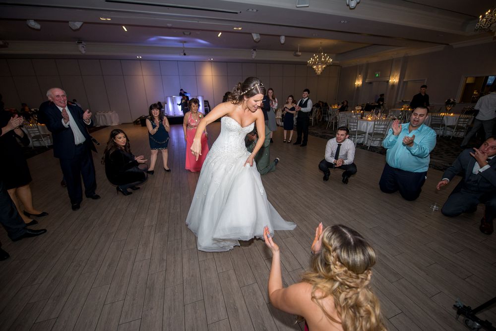 Bride in white gown dancing with guest on wedding reception dance floor.