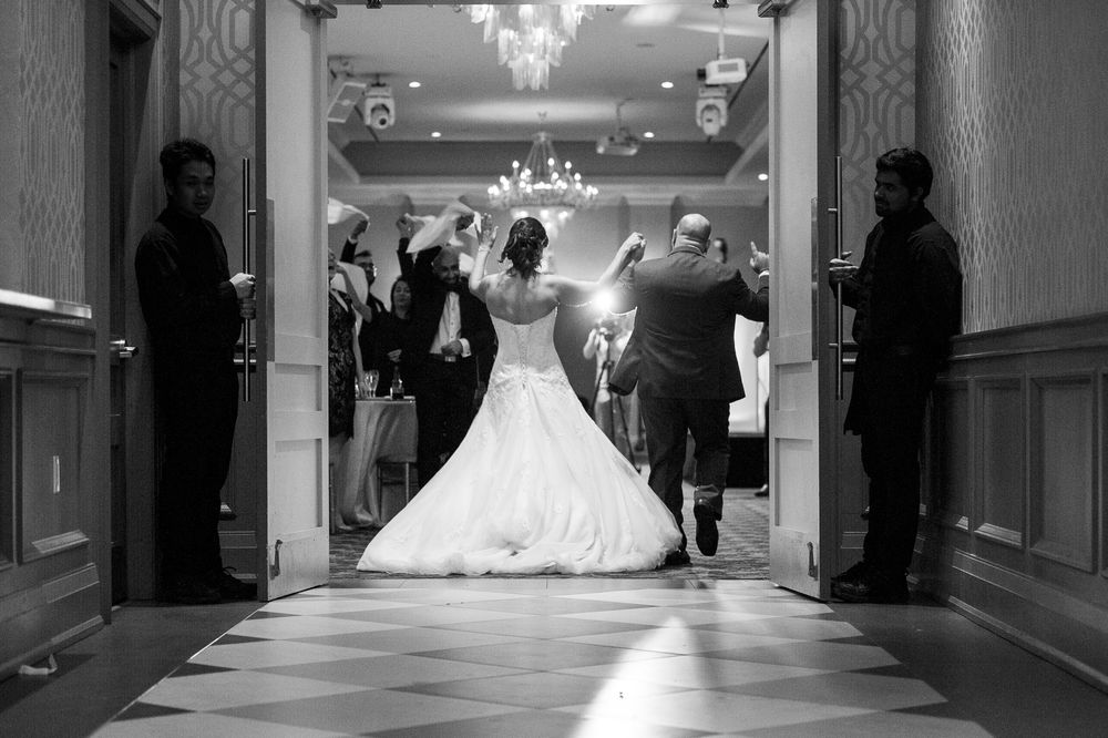 Black and white photo of bride in ball gown making grand entrance into wedding reception hall.