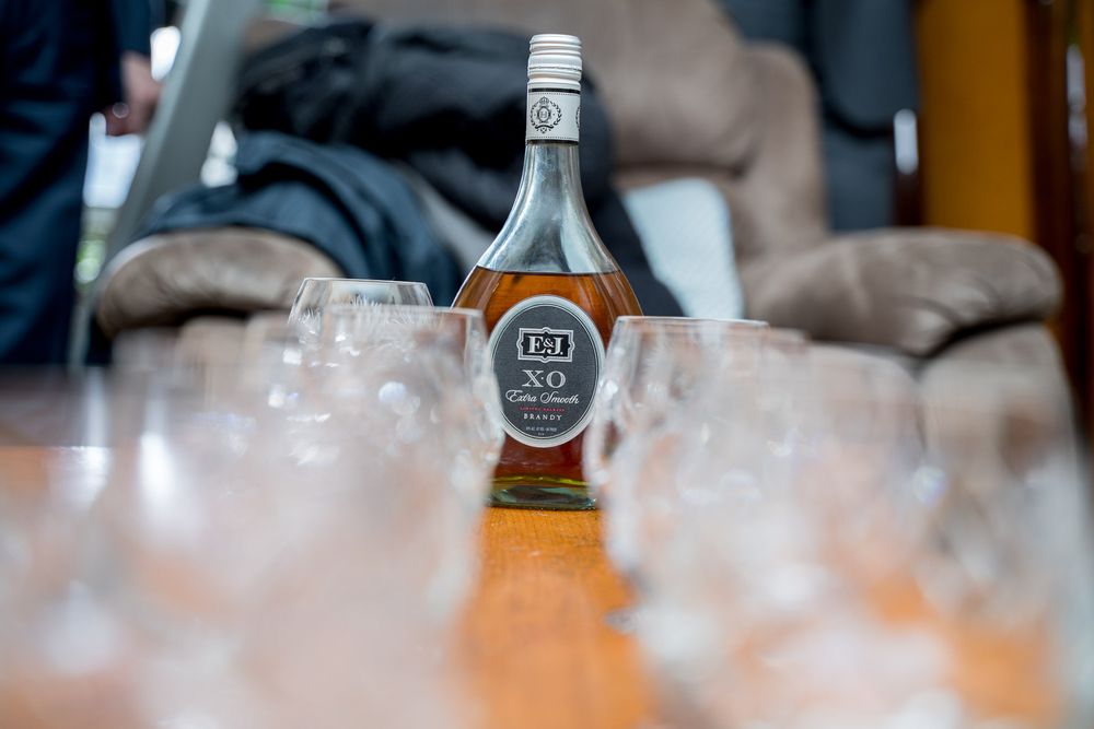 Bottle of XO brandy surrounded by empty crystal glasses on wooden table at wedding.