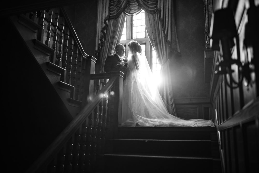 Black and white photo of bride and groom kissing on staircase with stunning lens flare.