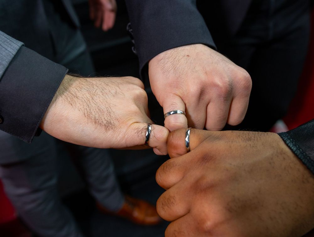 Three people wearing silver rings bump fists together in a show of unity and friendship.