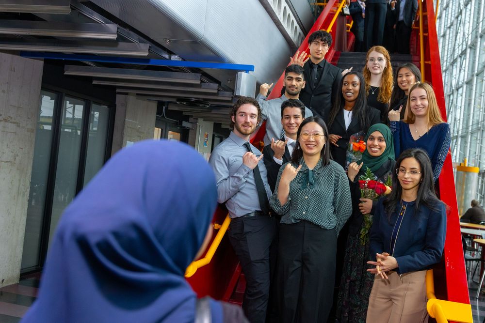 Diverse group of smiling students posing for a photo on an escalator in a modern building.