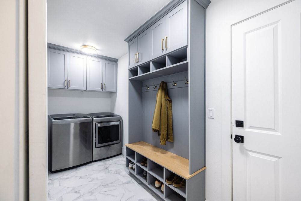 Organized mudroom with gray built-in lockers, bench, shoe storage, and stainless steel washer and dryer.