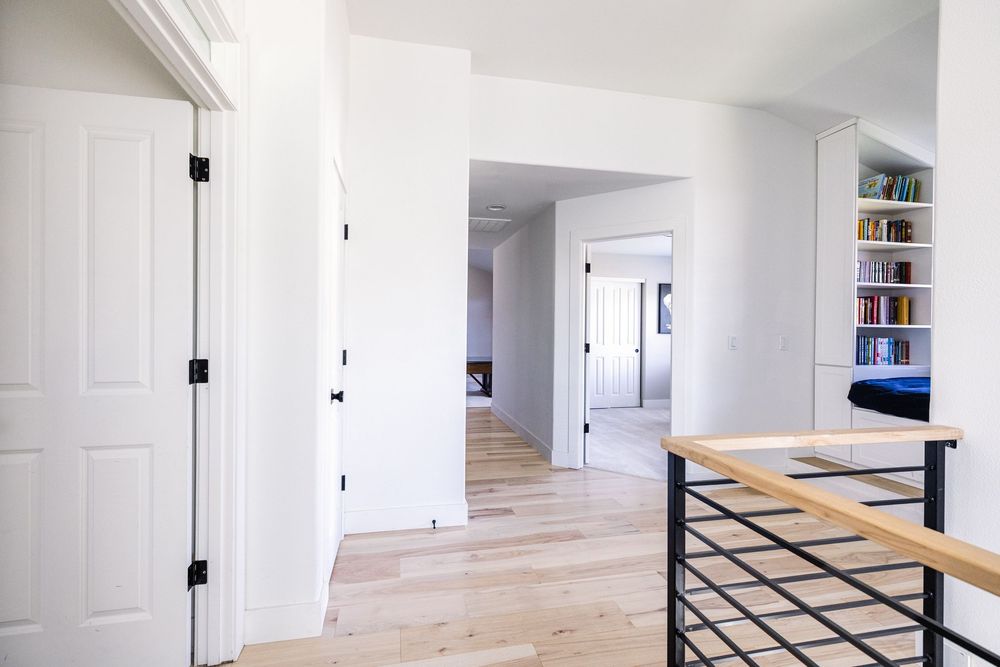 Bright upstairs hallway with white walls, black door hardware, hardwood floors, and built-in bookshelves.