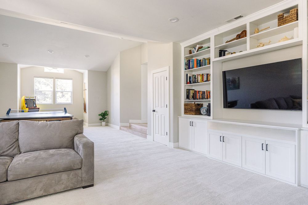 Bright upstairs living area with gray sofa, white built-in entertainment center, and open layout.