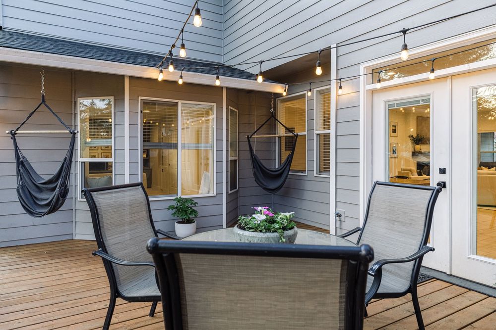 Cozy outdoor deck with string lights, hanging hammock chairs, and a patio dining set on wood planks.