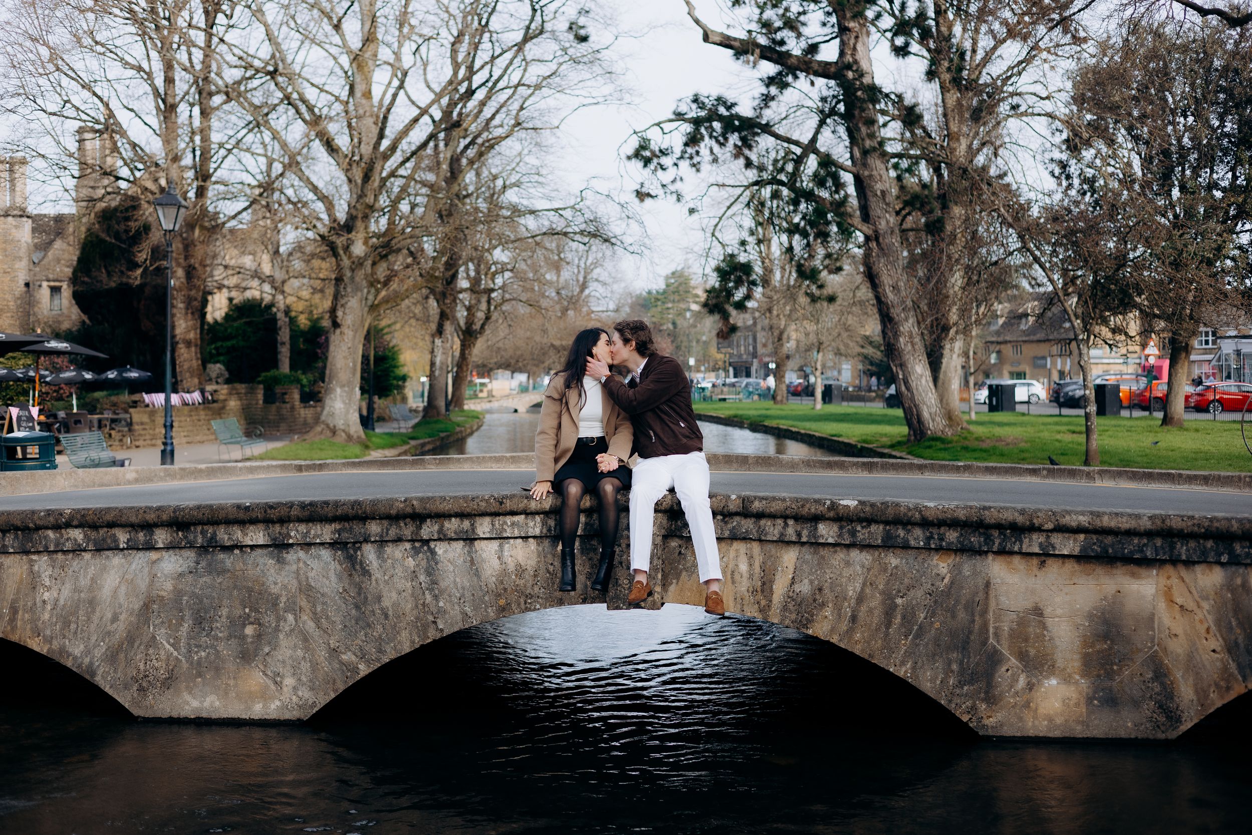 Couple sharing a romantic kiss on a stone bridge over a calm river in bourton on the water.