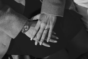 Black and white photo of two people stacking hands together, wearing a watch and diamond rings at a proposal photoshoot in the Cotswolds.