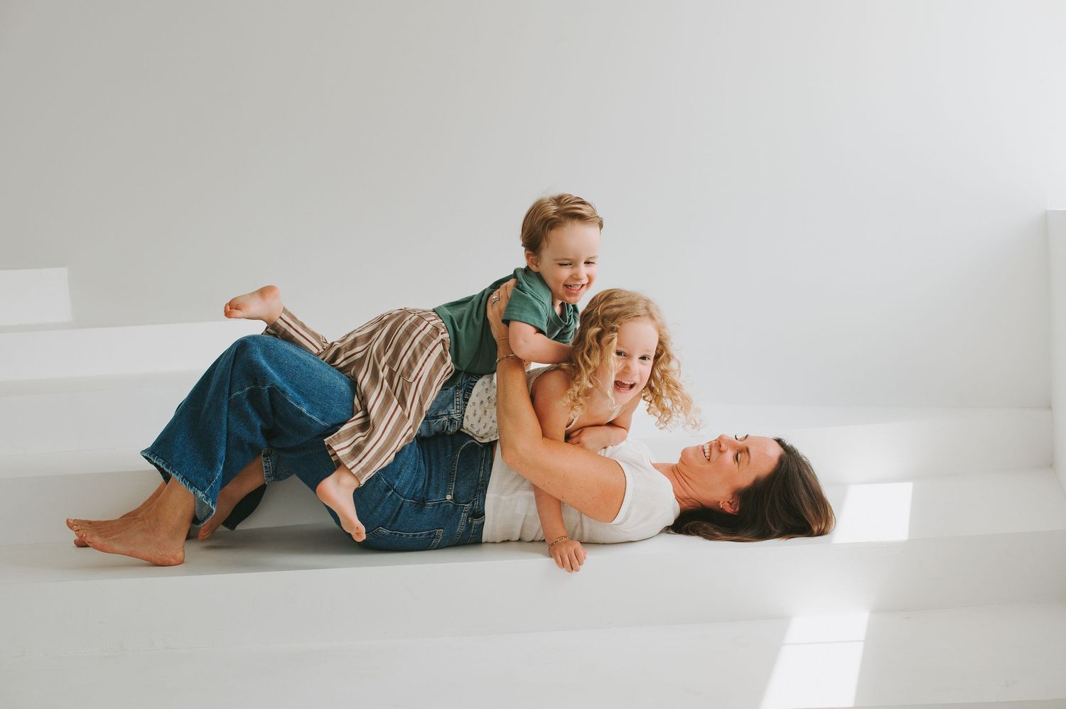 A joyful mother plays on the floor with two laughing children at Novi Haus photo studio in winter garden fl.