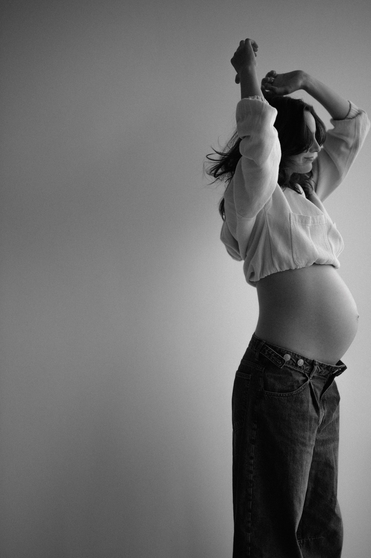 Black and white photo series showing a person in jeans and light top performing expressive dance movements against a plain wall.