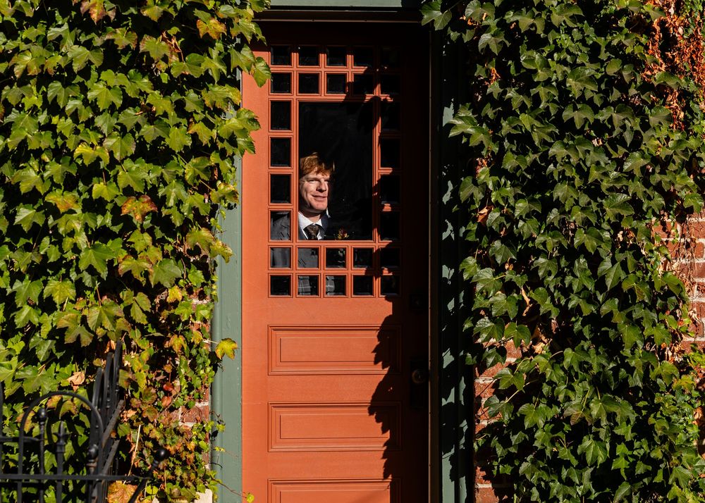 Person peering through a red latticed door surrounded by lush green ivy on a brick building exterior.
