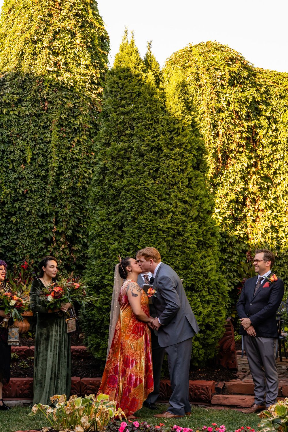 Bride and groom share first kiss in elegant outdoor garden wedding ceremony surrounded by greenery.