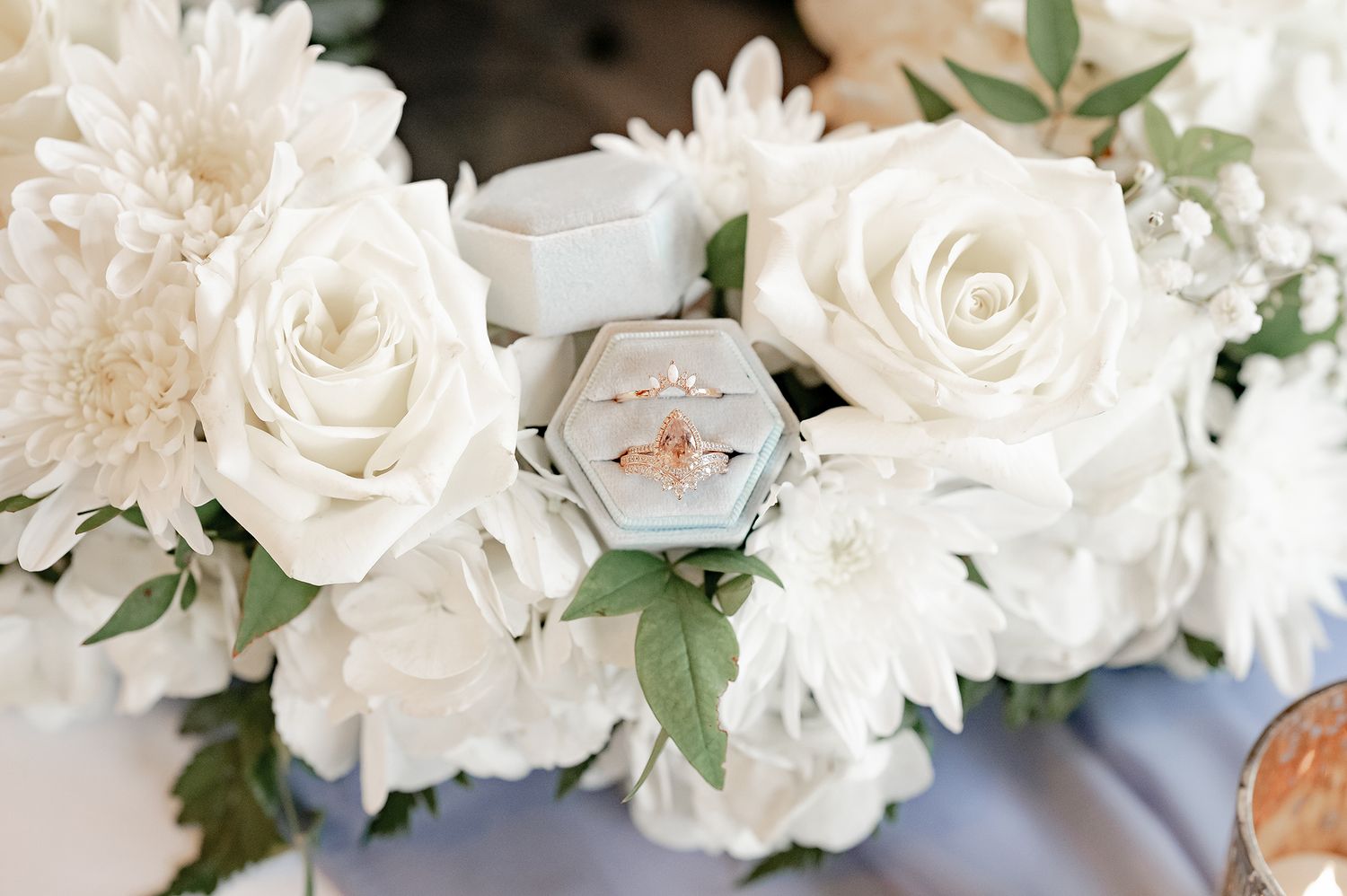 Rose gold engagement ring and wedding band displayed in hexagon box with white roses.