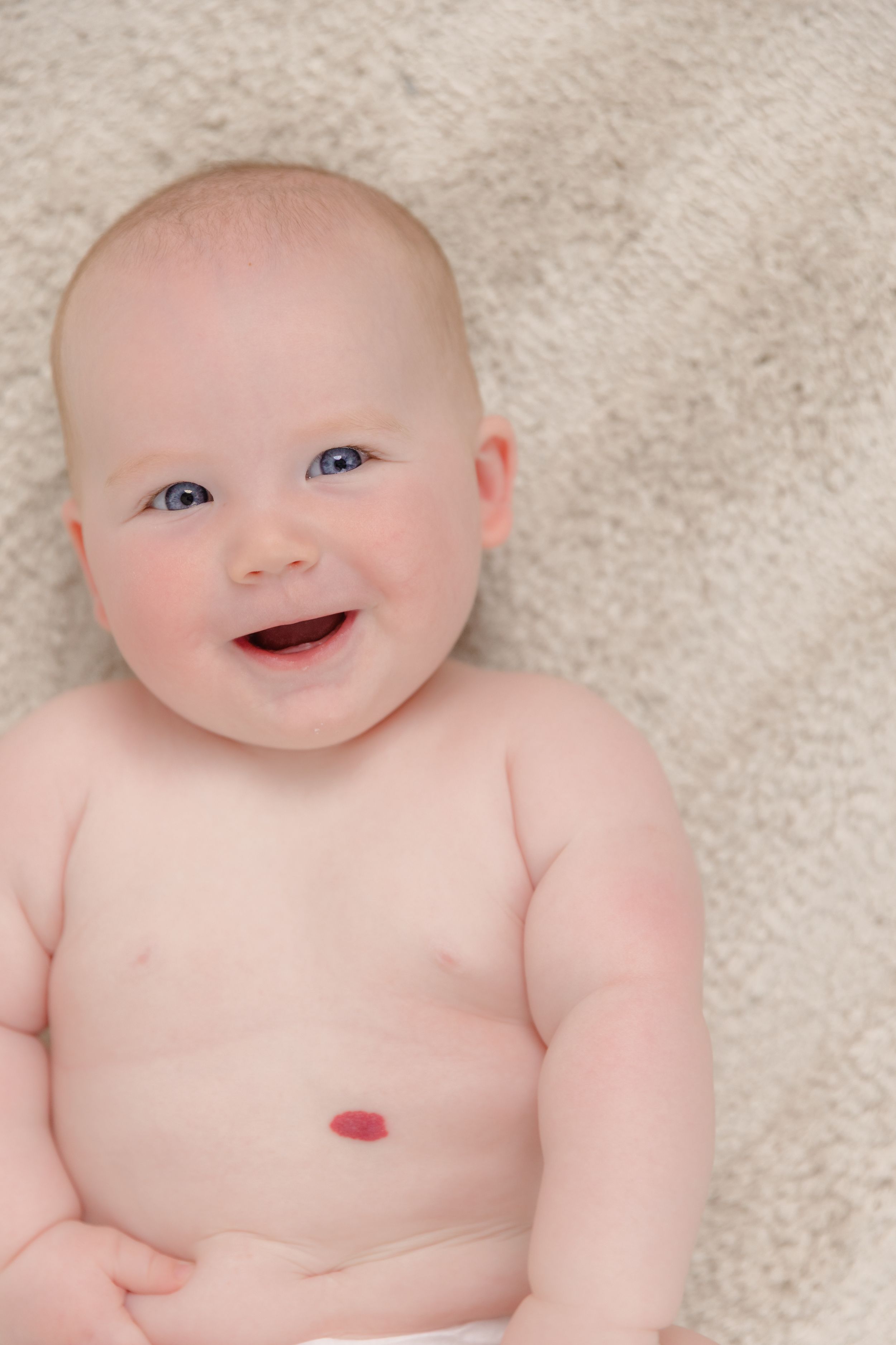 Happy smiling baby with blue eyes sitting up on a soft cream blanket.