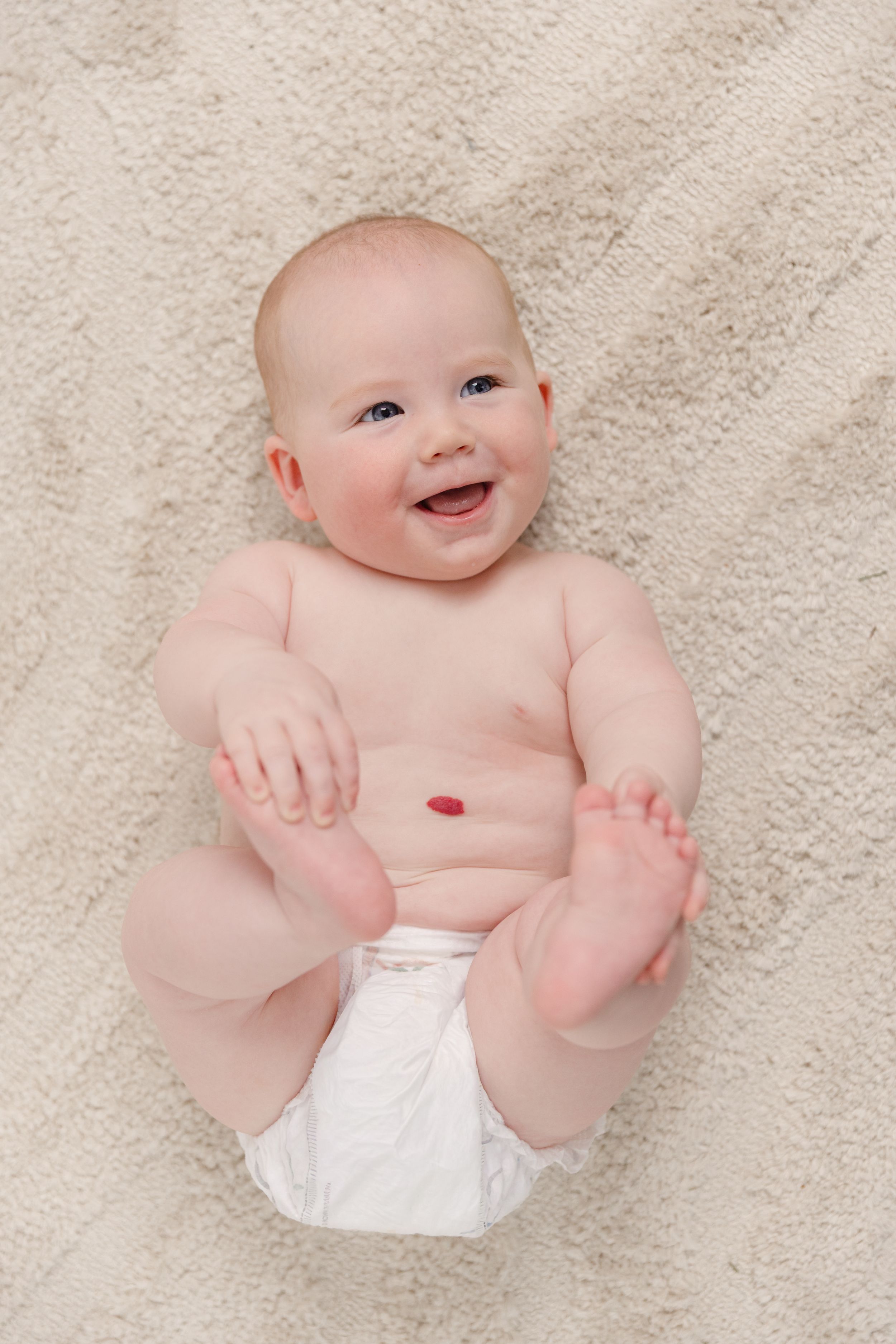 Happy baby in white diaper laughing while lying on a soft beige blanket.