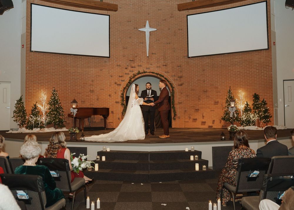 Bride and groom exchange vows at a church altar decorated with Christmas trees and candles.