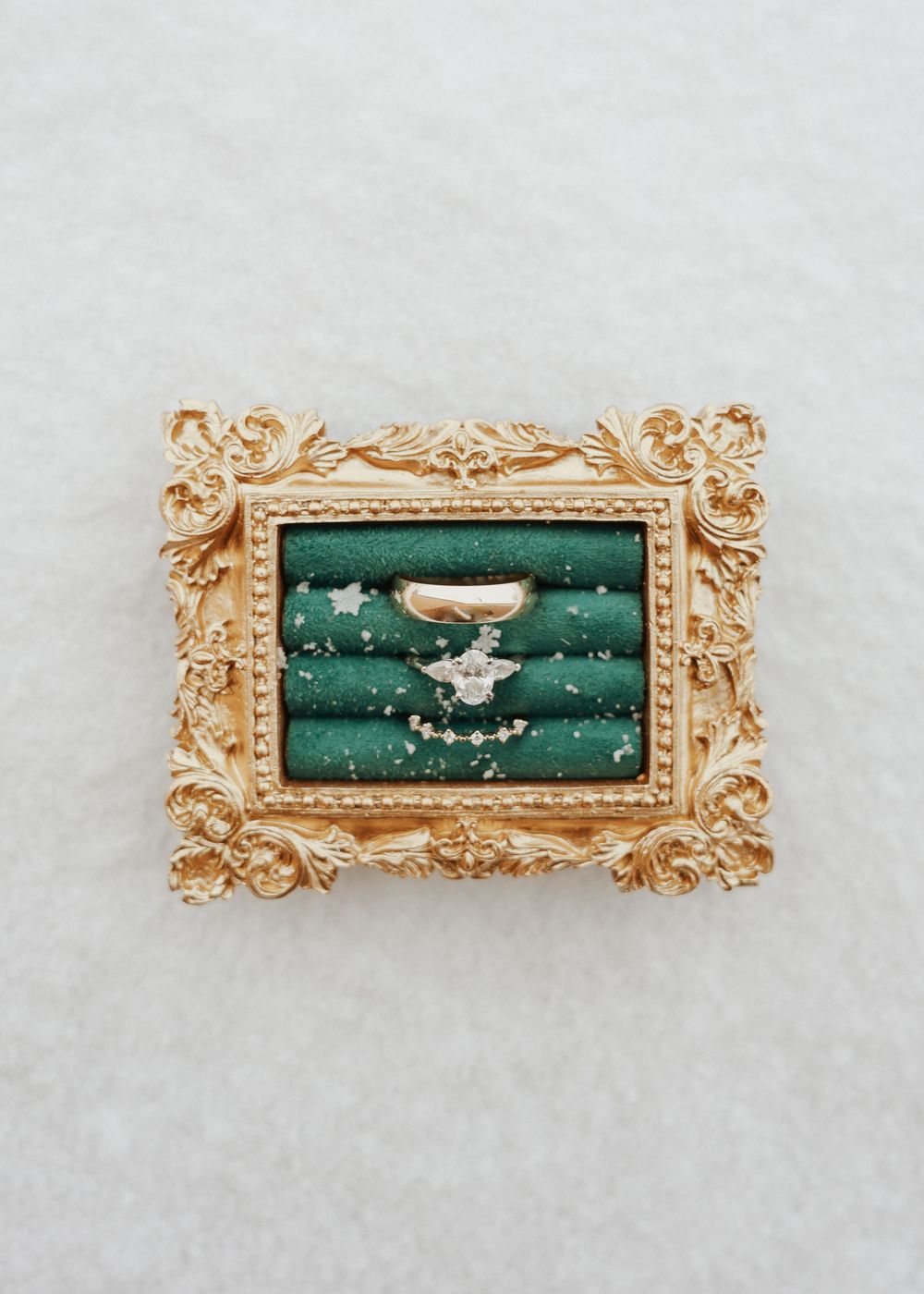 Elegant diamond engagement ring displayed in an ornate gold frame with green velvet lining.