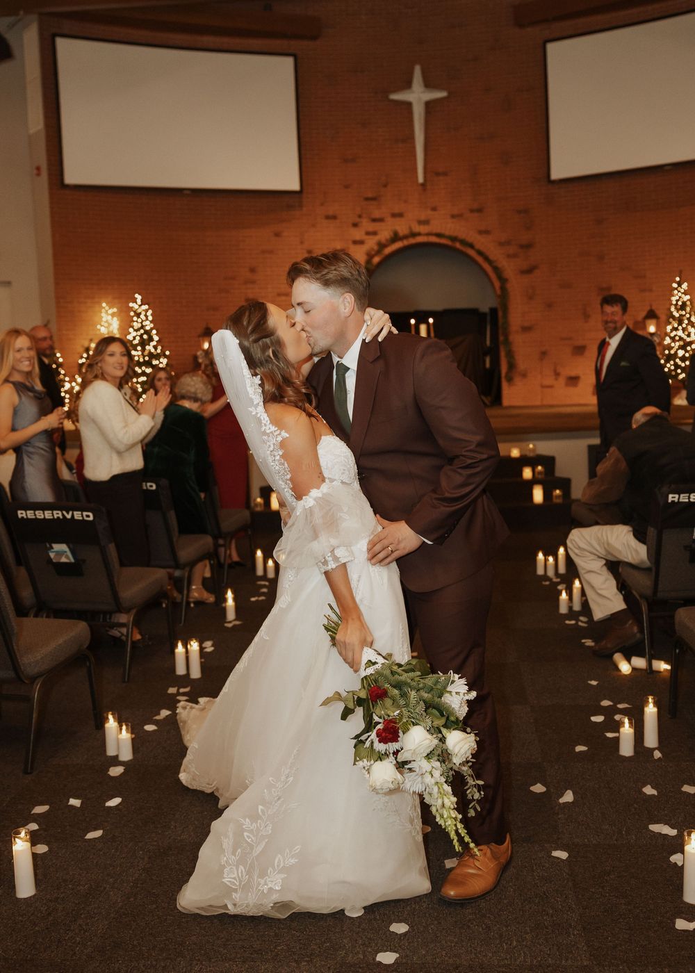Newlyweds share a first kiss in the candlelit church aisle after their winter wedding ceremony.