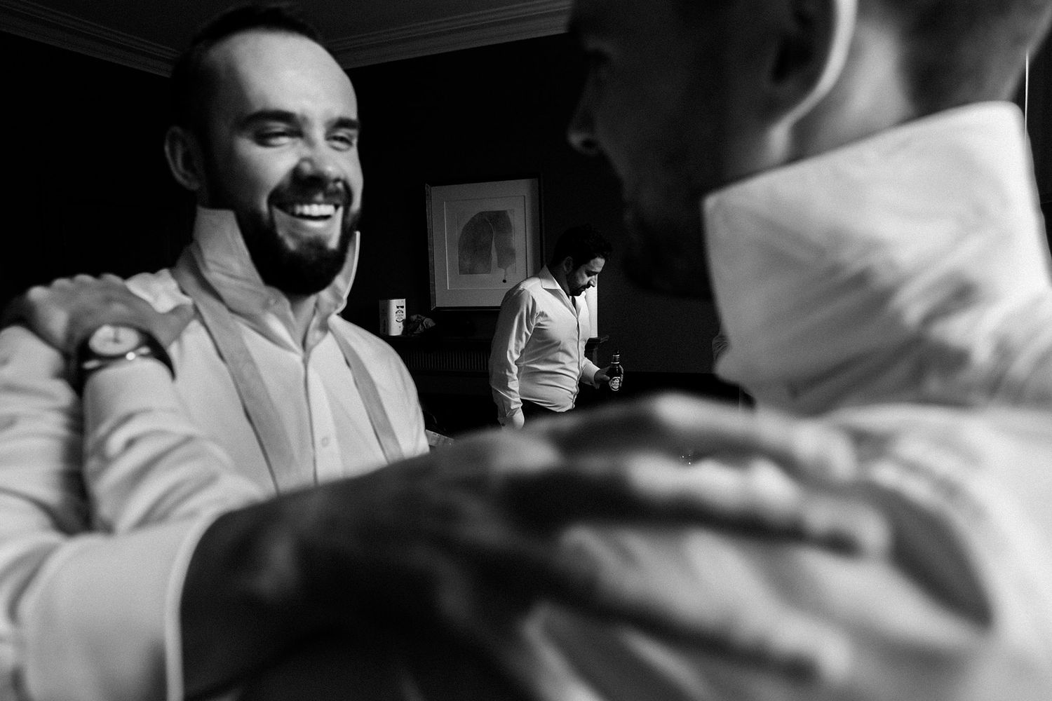 Black and white photo of two grooms smiling and sharing a joyful moment while getting ready for their wedding.
