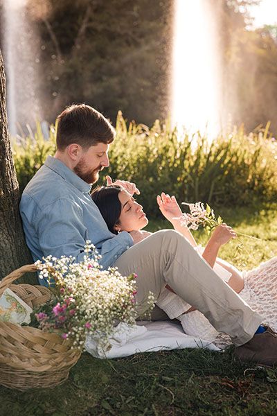 Couple enjoys romantic picnic in sunlit meadow in Vondelpark with wildflowers and wicker basket at sunset.