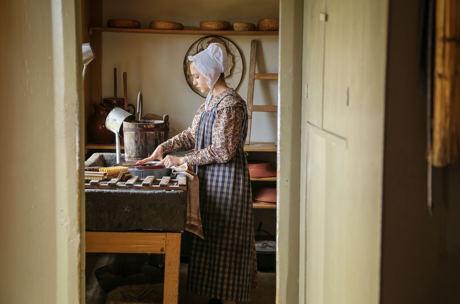 Colonial woman in kitchen washing dishes in low, soft light at Sturbridge Village Massachusetts historical setting. New England photographer