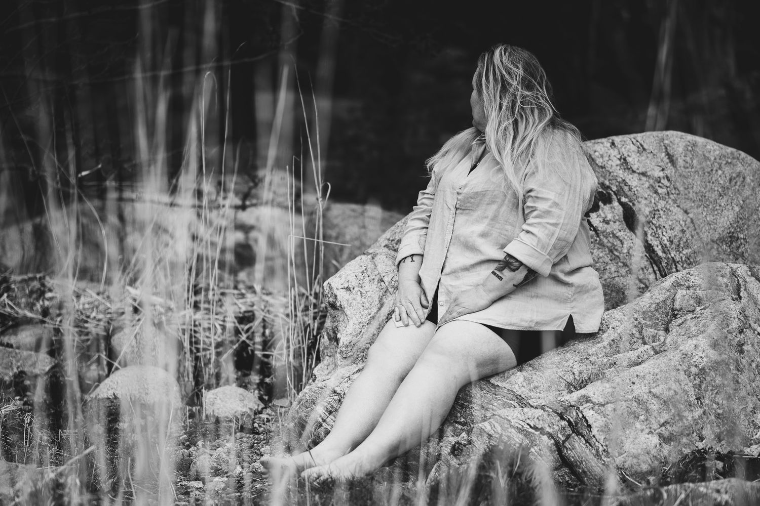 Svartvitt porträttfoto av Fotograf Jessica Lindqvist - en kvinna som sitter barfota på en klippa, blickandes bort.