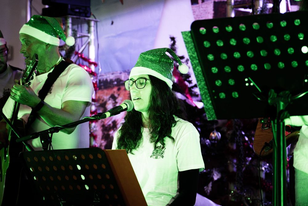 Musician wearing green elf hat performs at keyboard during festive Christmas concert under green stage lights.