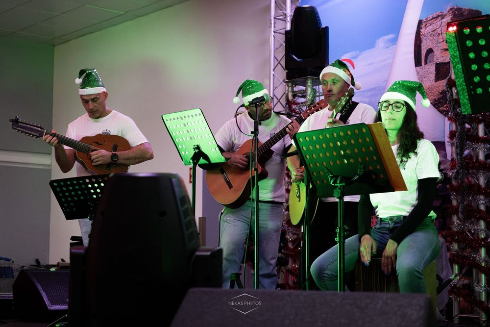 Four musicians wearing Santa hats perform with guitars at a Christmas event under green stage lighting.