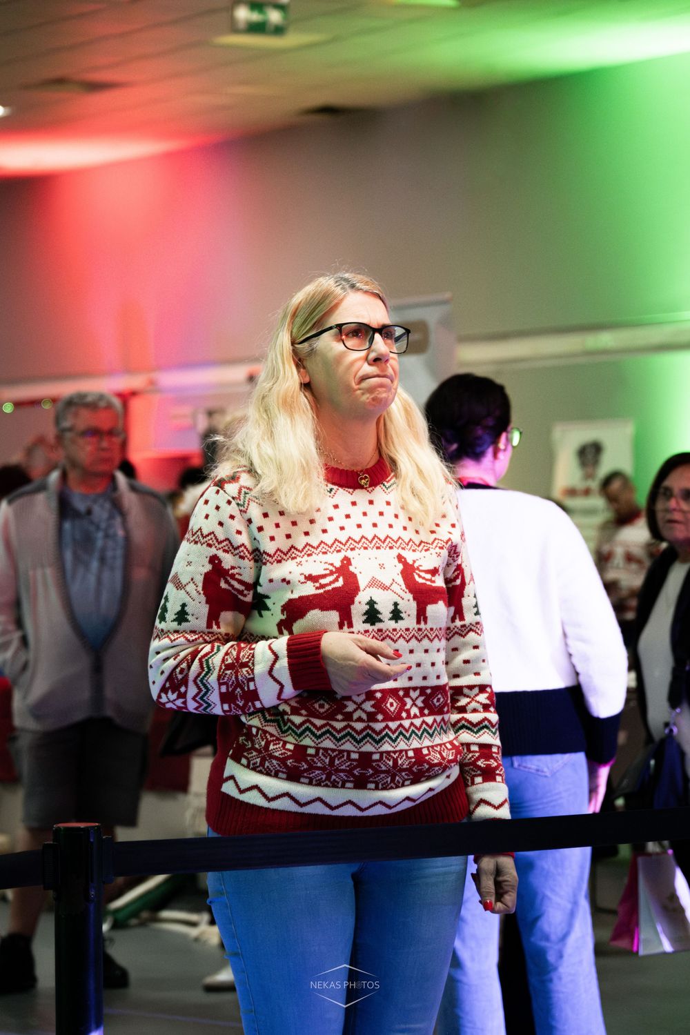 Woman in festive Christmas sweater with reindeer pattern standing in queue at holiday event.