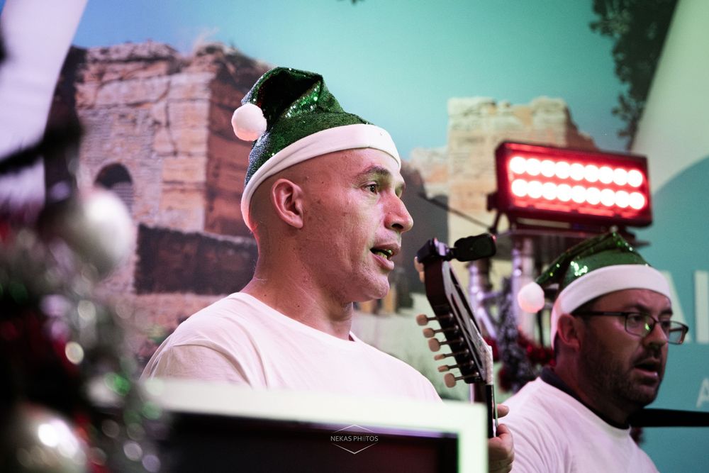 Two men wearing Santa hats perform at a Christmas music event indoors.