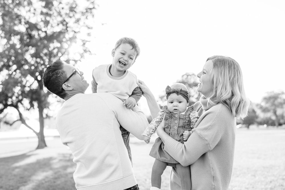 Black and white photo of joyful family with two children playing outdoors in sunny park.