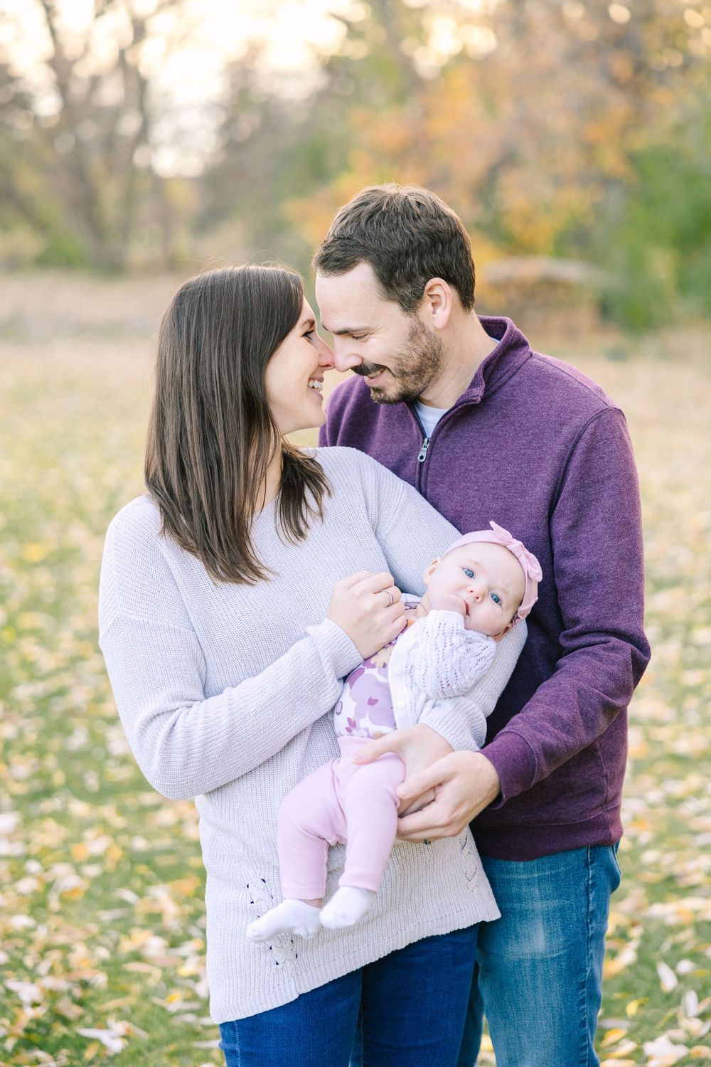 Smiling couple in autumn park sharing a tender moment while holding their newborn baby.