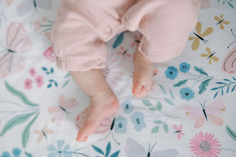 Close-up of a newborn baby's tiny feet resting on a floral butterfly patterned blanket.