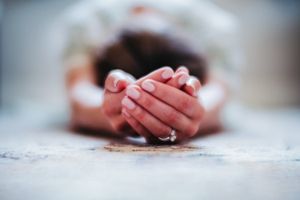 Person kneeling in prayer with hands clasped together on a marble surface in a devotional pose.