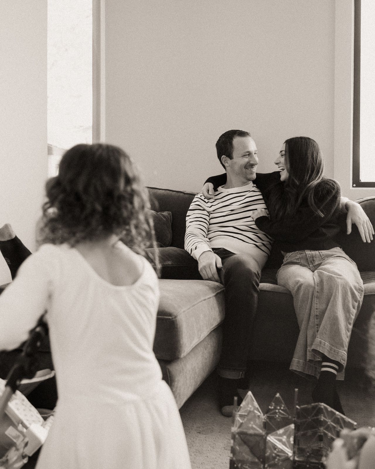 Black and white photo of a couple sitting on a couch smiling at each other during a holiday gift exchange.