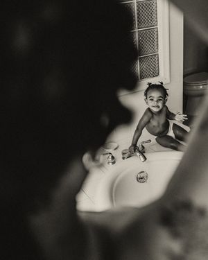 Black and white photo of a happy baby sitting in a bathroom sink, smiling at the camera.