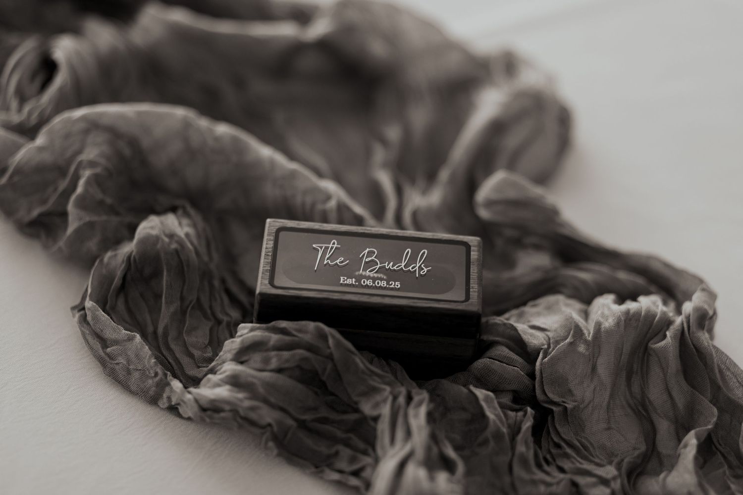 Gray silk scrunchie beside a dark branded box labeled The Bandels on a white surface.